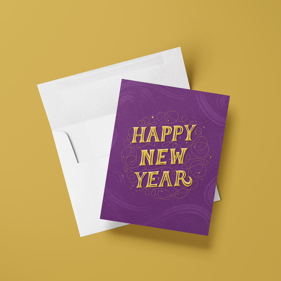 Purple 'Happy New Year' card with gold text on a white envelope against a mustard yellow background
