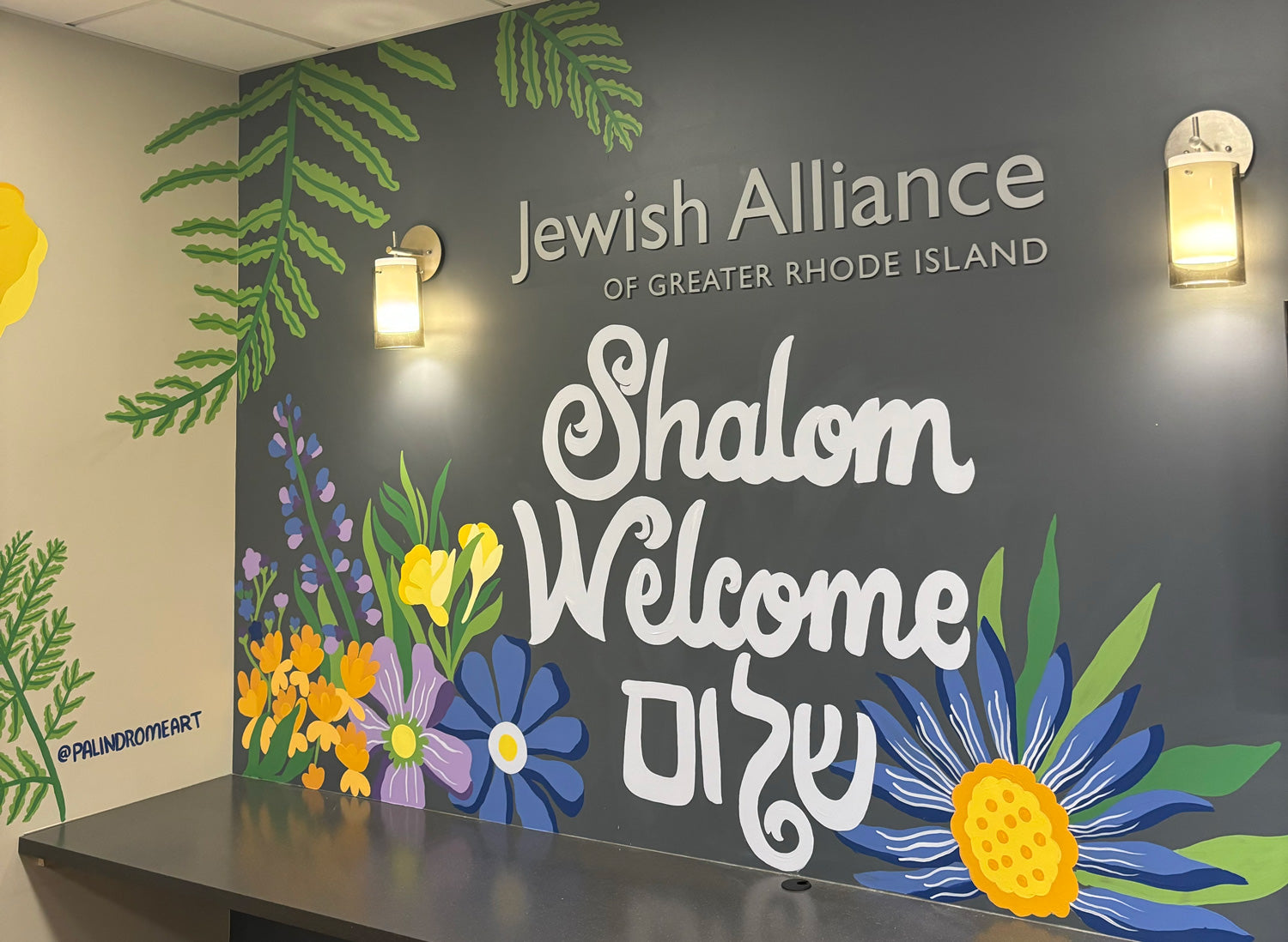 Wall with 'Jewish Alliance of Greater Rhode Island' sign and floral mural decorations.