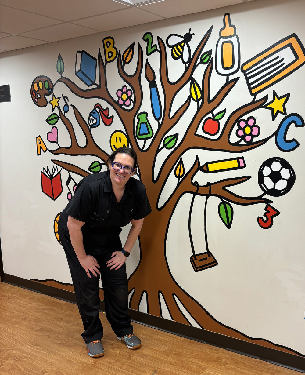 Person standing in front of a colorful wall mural of a tree with educational symbols