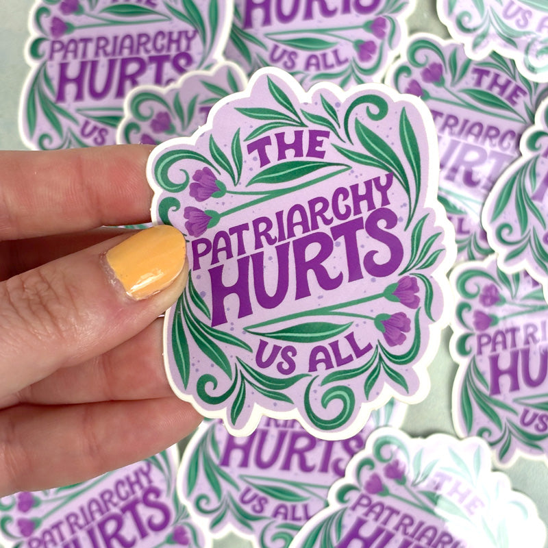 A sticker with a purple background and the text 'THE PATRIARCHY HURTS US ALL' along with floral designs.
