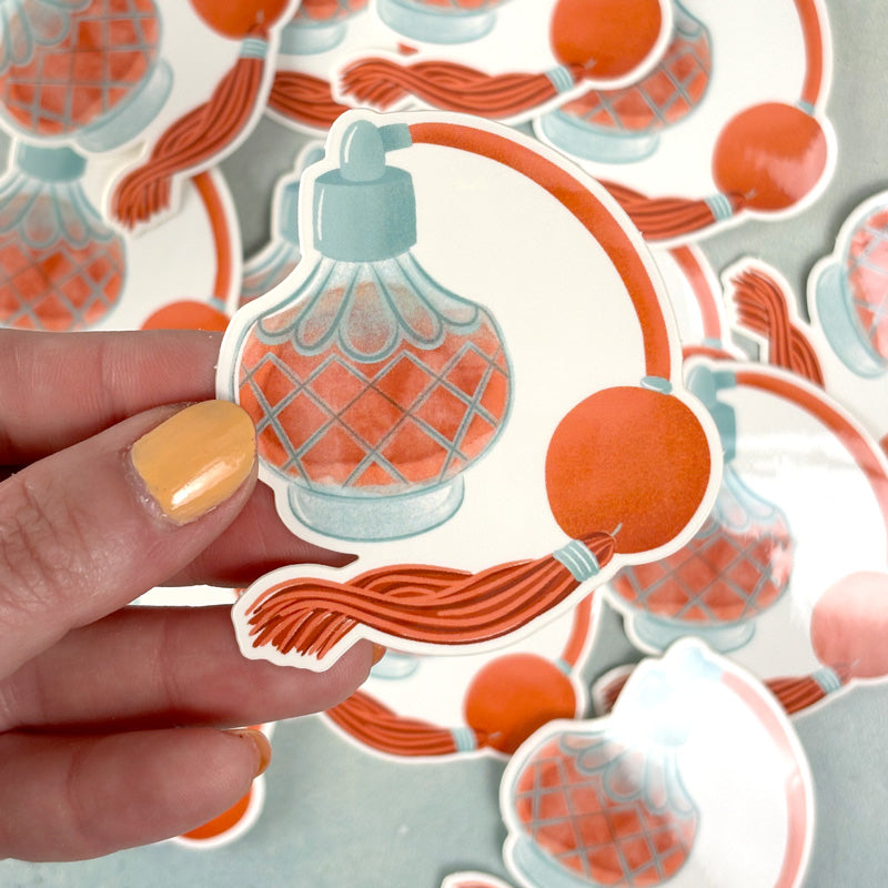 hand holding A decorative sticker featuring a stylized pink and orange perfume bottle with a pump and a red ribbon.