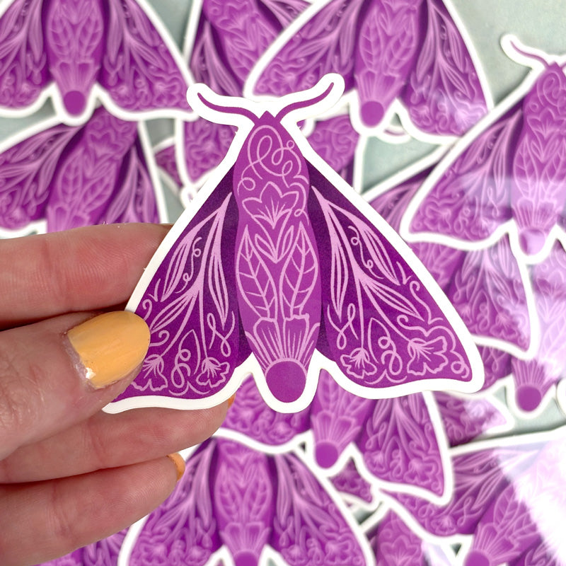 hand holding A purple sticker featuring a moth with floral patterns 