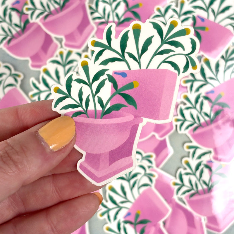 hand holding A sticker depicting a pink toilet bowl filled with green plants.