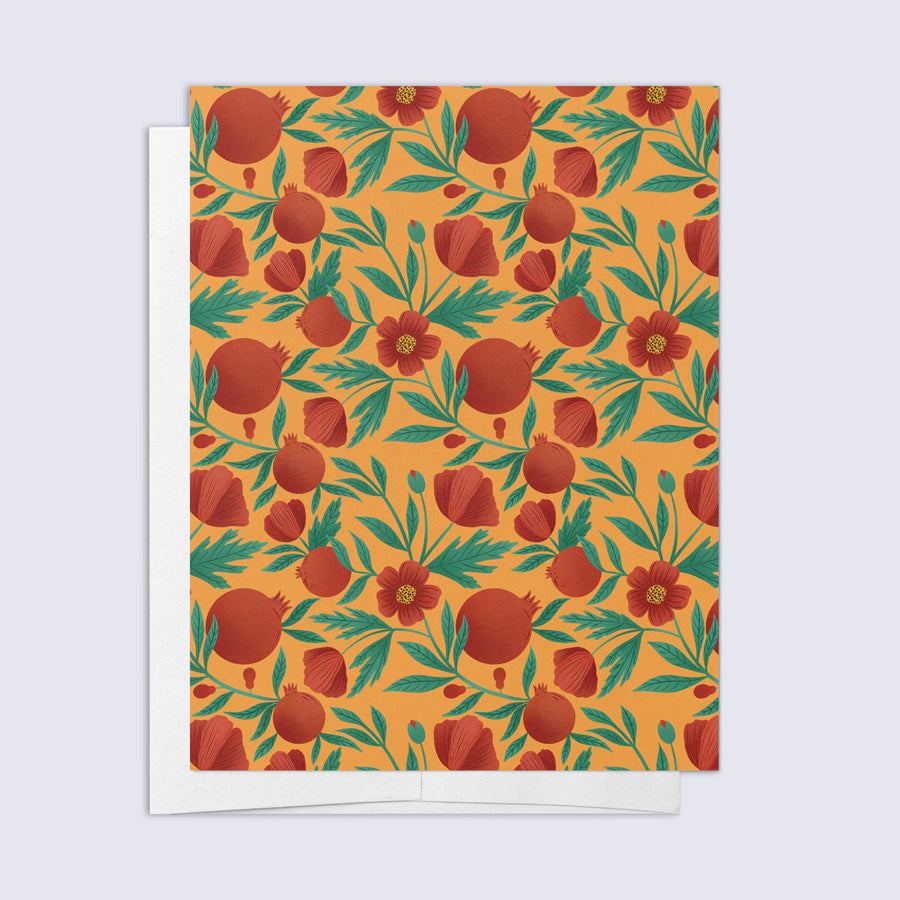 A greeting card with a floral pattern featuring pomegranates and poppies, in shades of orange, red, and green, with a blank inside and a bright white envelope.