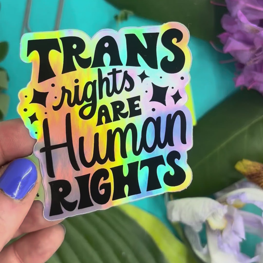 hand holding a holographic vinyl sticker that says "trans rights are human rights"