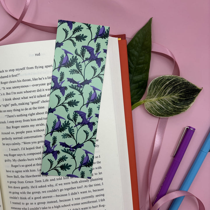 bookmark featuring purple pterodactyl dinosaurs and leafy plants in an open book