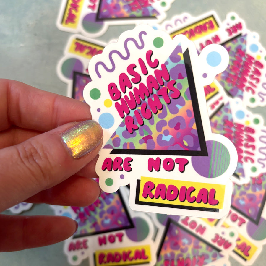 Sticker with 'Basic Human Rights Are Not Radical' text held by a hand with colorful nail polish, with more stickers in the background.
