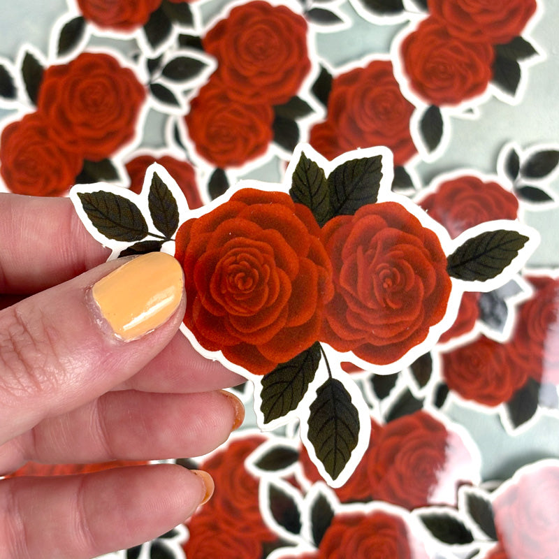 A sticker with an illustration of a red rose with dark green leaves