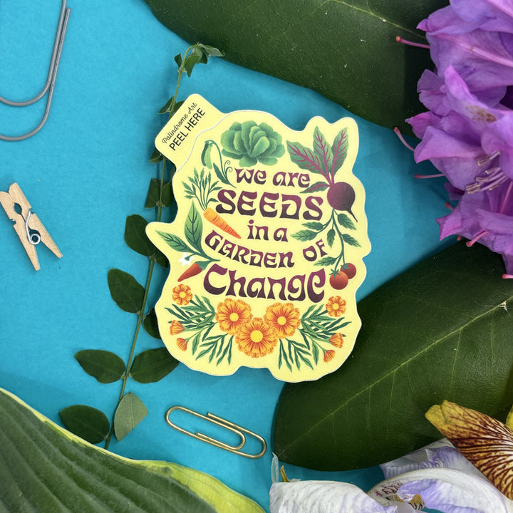 Sticker with 'We are seeds in a garden of change' text on a blue background with leaves and flowers.