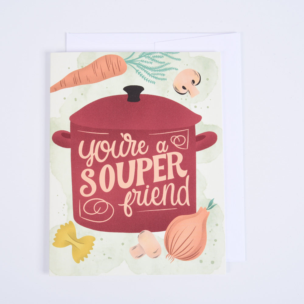 A folded greeting card with a red pot and vegetables on the front, with the text 'You're a souper friend' 