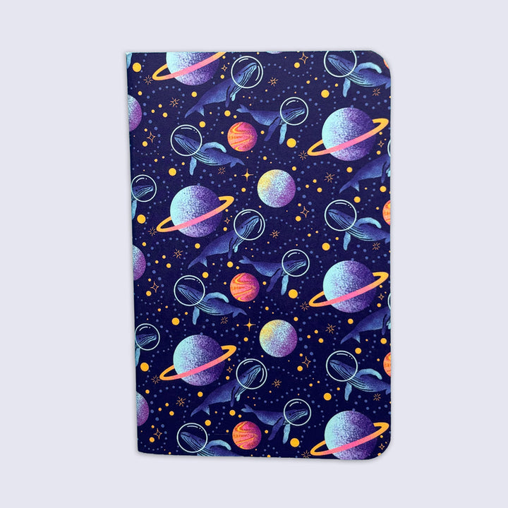 a small notebook with rounded corners featuring illustrations of whales with space helmets exploring space amid planets and stars