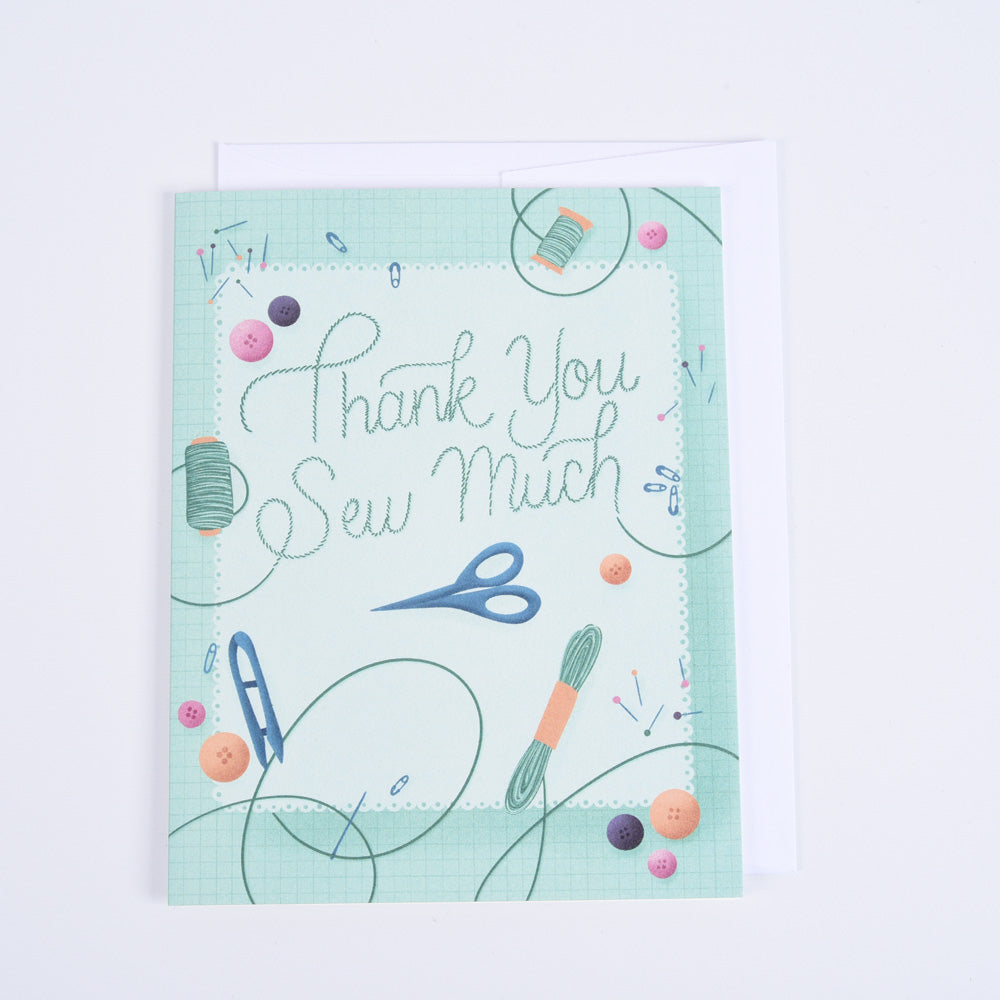 A folded greeting card with a colorful design featuring sewing-related images such as scissors, thread, and fabric, with the text 'Thank You Sew Much'.