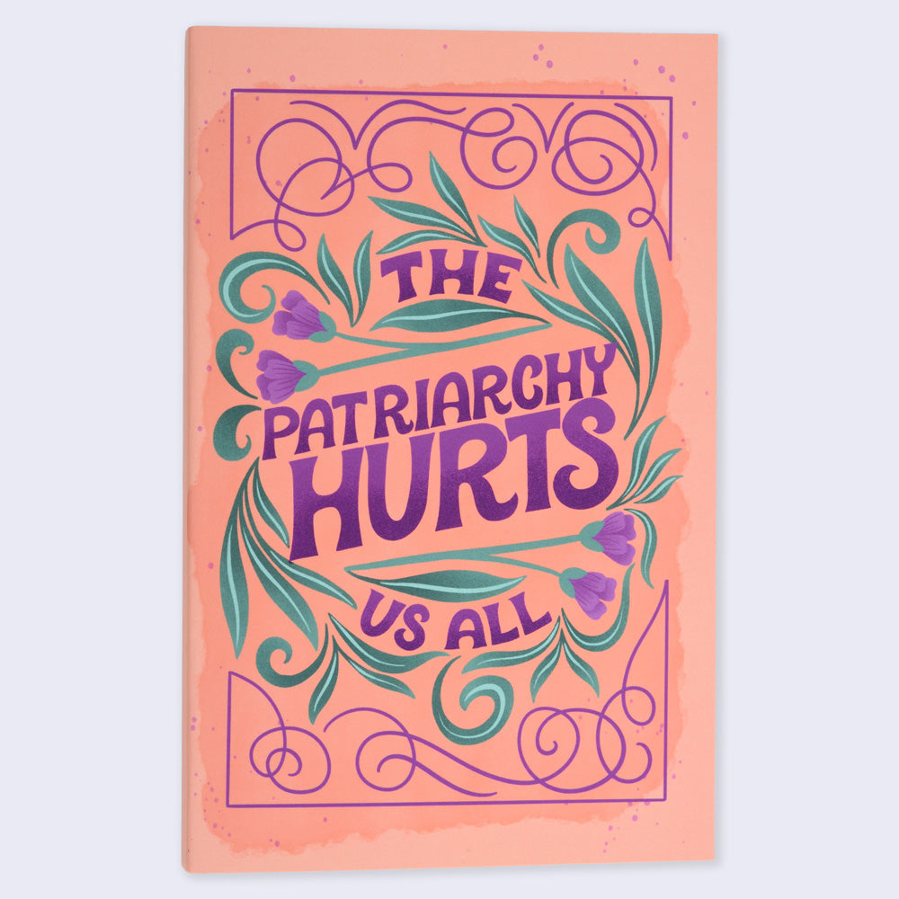 A flat lay image of a notebook with an orange cover featuring a purple-colored floral and text design, with the title 'THE PATRIARCHY HURTS US ALL' written on it.