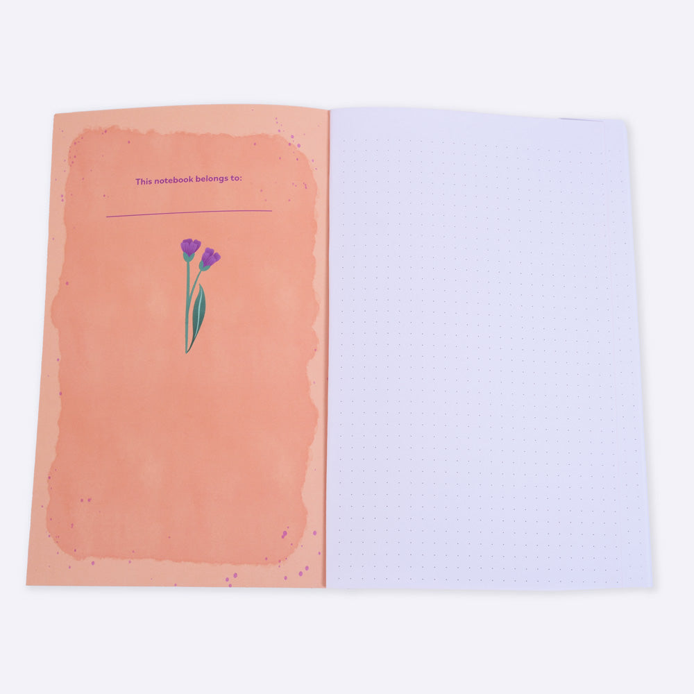 open flat lay notebook with dot grid pages, the left inside cover is orange with text "this notebook belongs to"