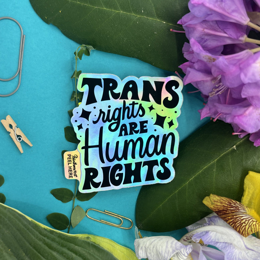 Holographic sticker with 'Trans rights are human rights' text on a blue background with flowers and leaves.