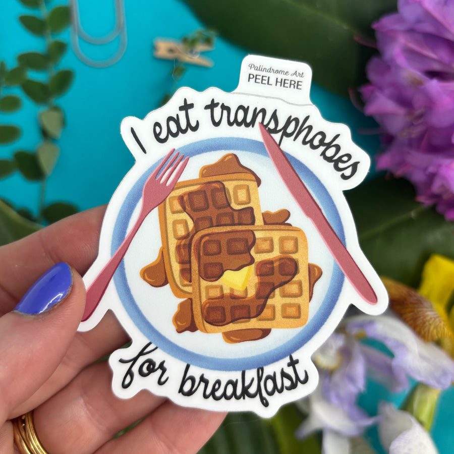 Sticker with waffle design and text "I eat transphobes for breakfast" held by a hand against a colorful background