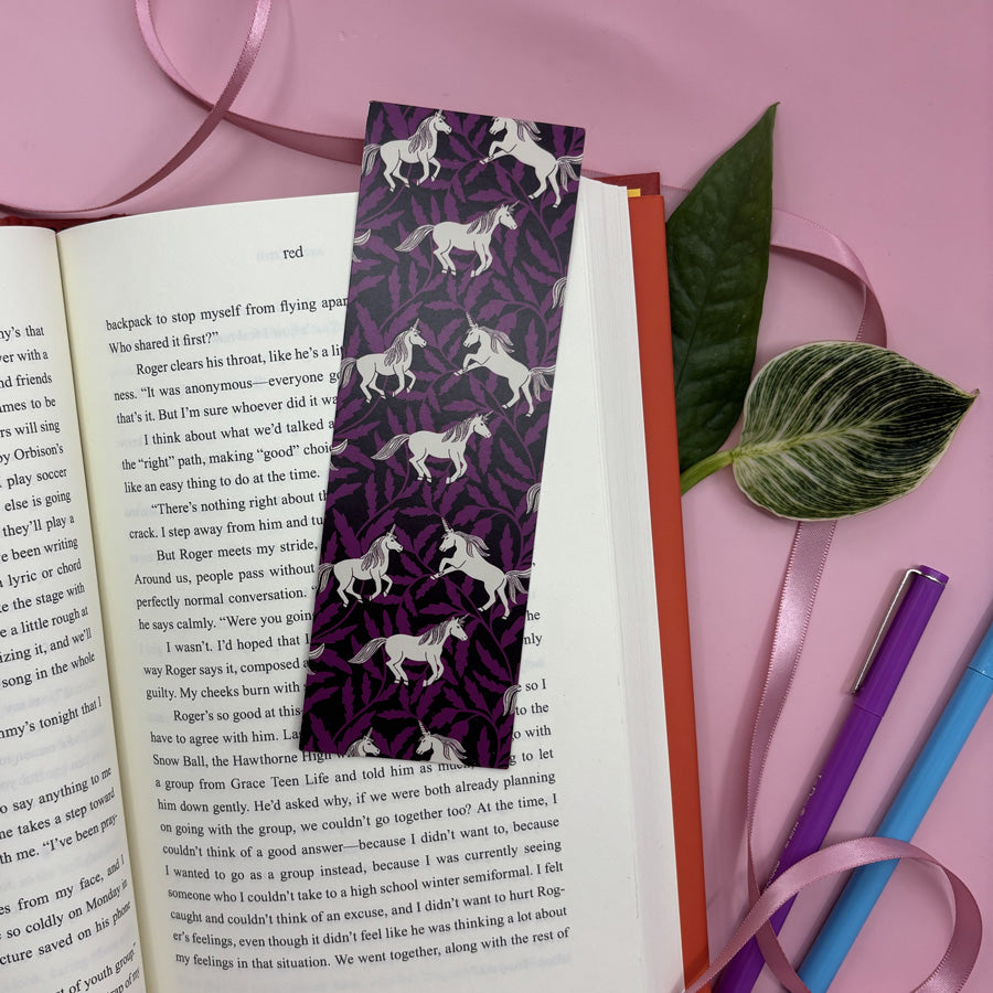 Unicorn-patterned bookmark on an open book with stationery items on a pink background