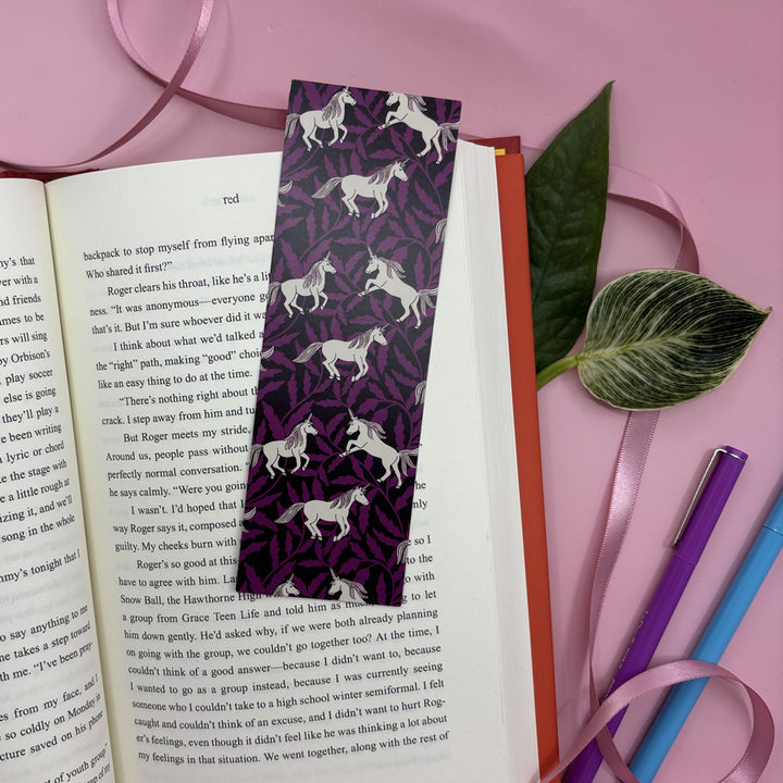 Unicorn-patterned bookmark on an open book with stationery items on a pink background