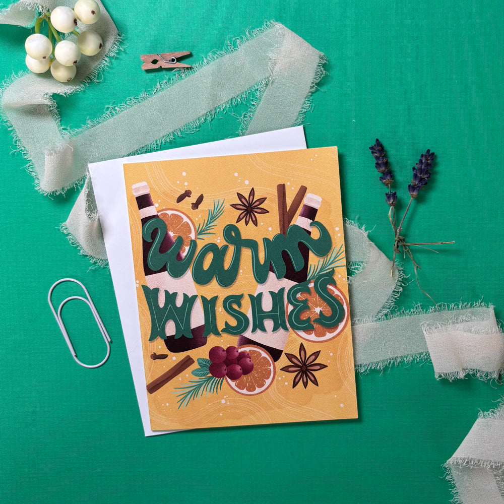 Greeting card with 'Warm Wishes' and mulled wine ingredients on a green background with decorative elements.