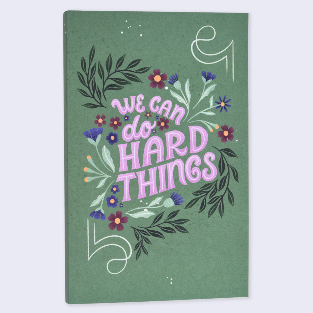 notebook with a green cover and flower illustrations that says "we can do hard things"