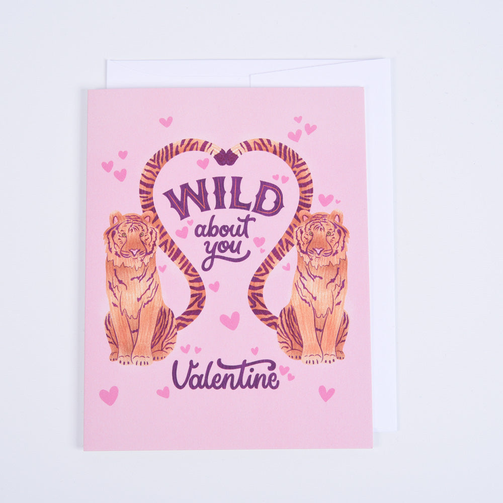 A pink folded greeting card with 'Wild About You' text and illustrations of two tiger stripes, paired with a bright white envelope.